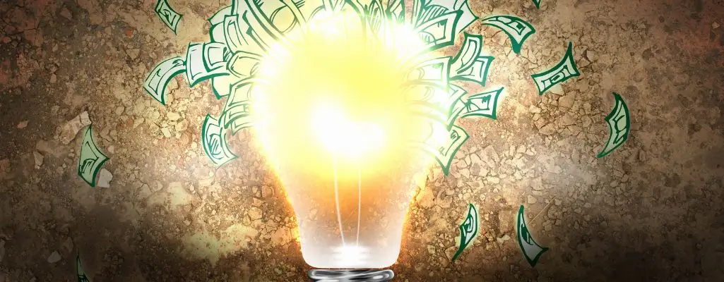 Zdjęcie w artykule - Jak zarobić pieniądze? Widoczna świecąca żarówka, w tle fruwają banknoty.