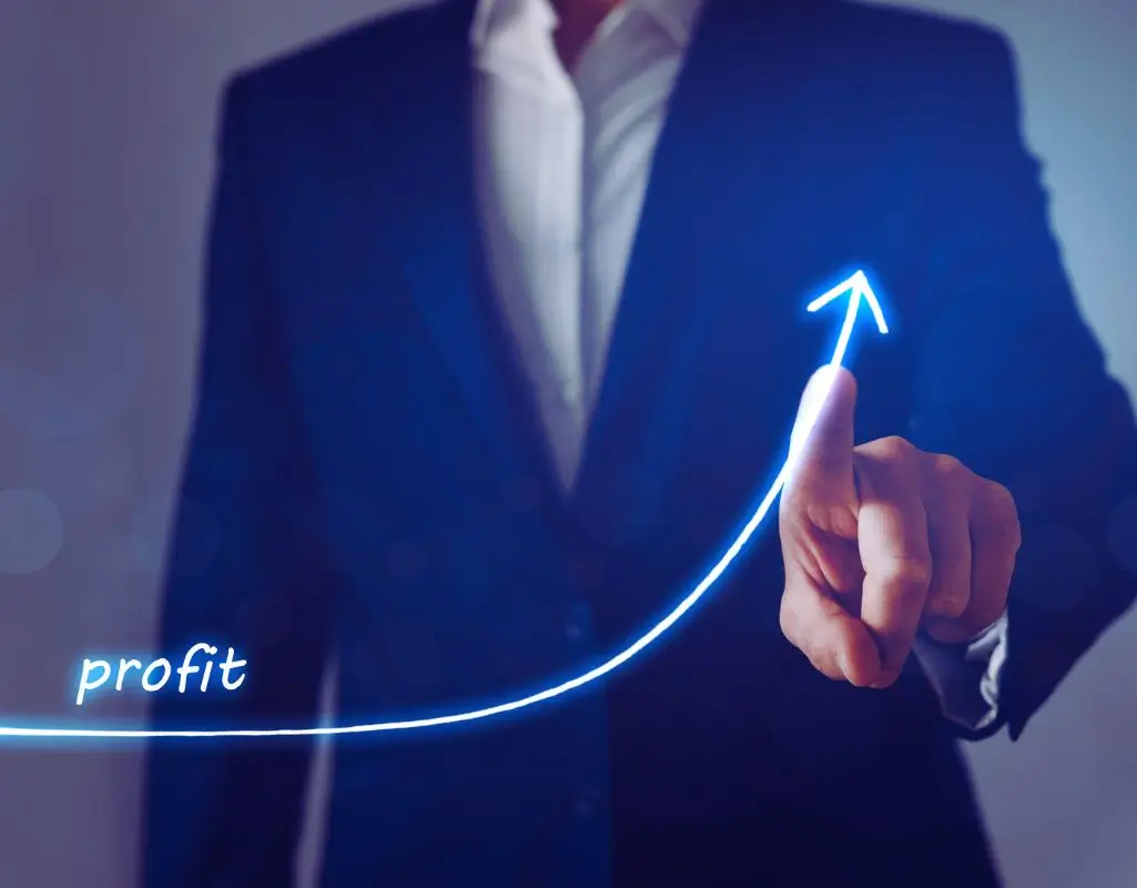 Na obrazie widać mężczyznę w garniturze, który delikatnie dotyka świecącej, niebieskiej linii wzrostu. Linia ta symbolizuje wykres rosnących wyników i kończy się strzałką skierowaną w górę. Na jej początku znajduje się napis „profit”, czyli zysk. Całość emanuje poczuciem profesjonalizmu, nowoczesności i sukcesu. Zdjęcie sugeruje dynamiczny rozwój i pozytywne zmiany, jakie może przynieść dobra decyzja biznesowa — w tym korzyści z zatrudnienia osoby niepełnosprawnej, które mogą mieć realny wpływ na wzrost wartości firmy.